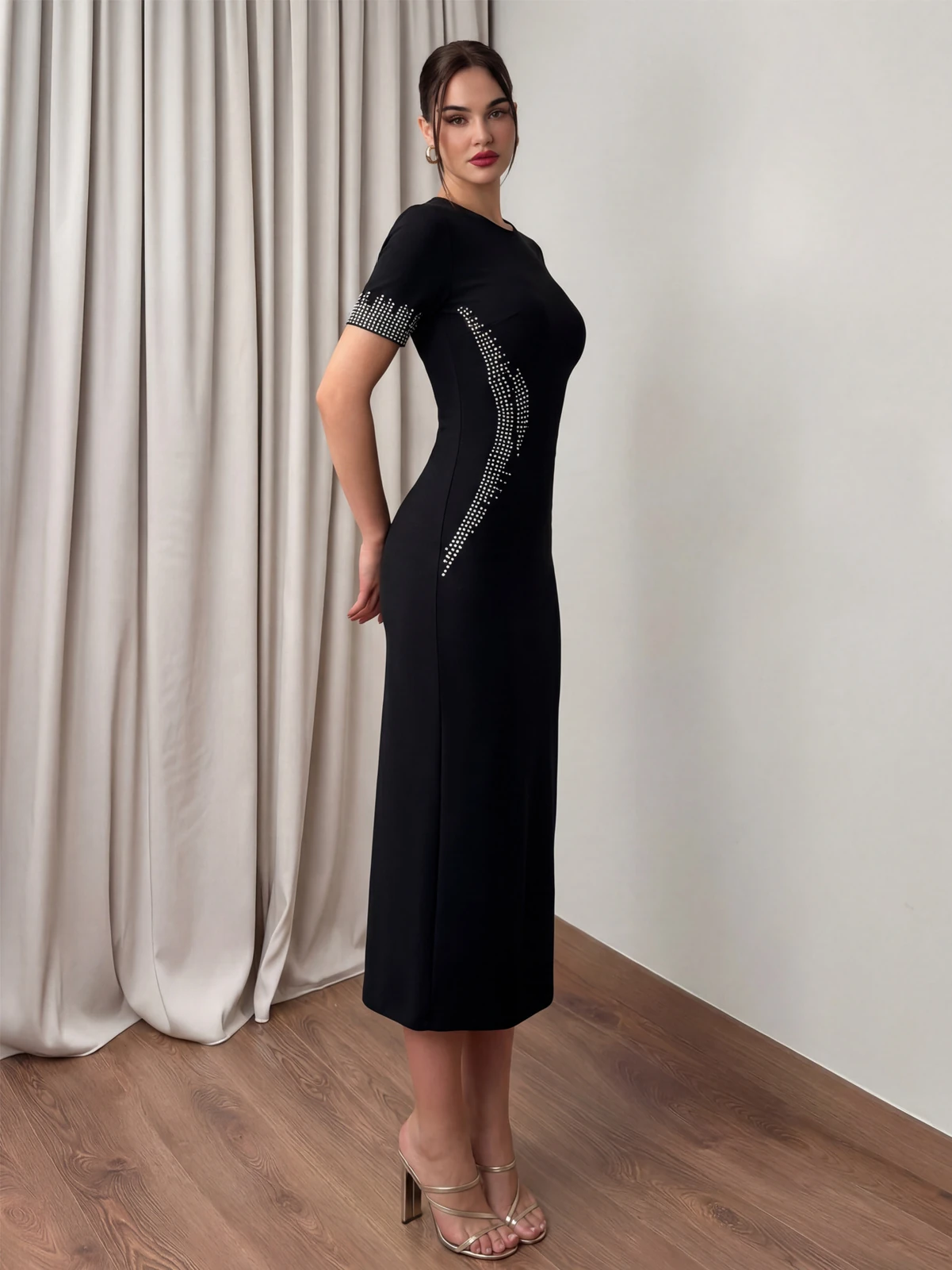 Side view of black short sleeve bandage dress with rhinestone trim on sleeve and side