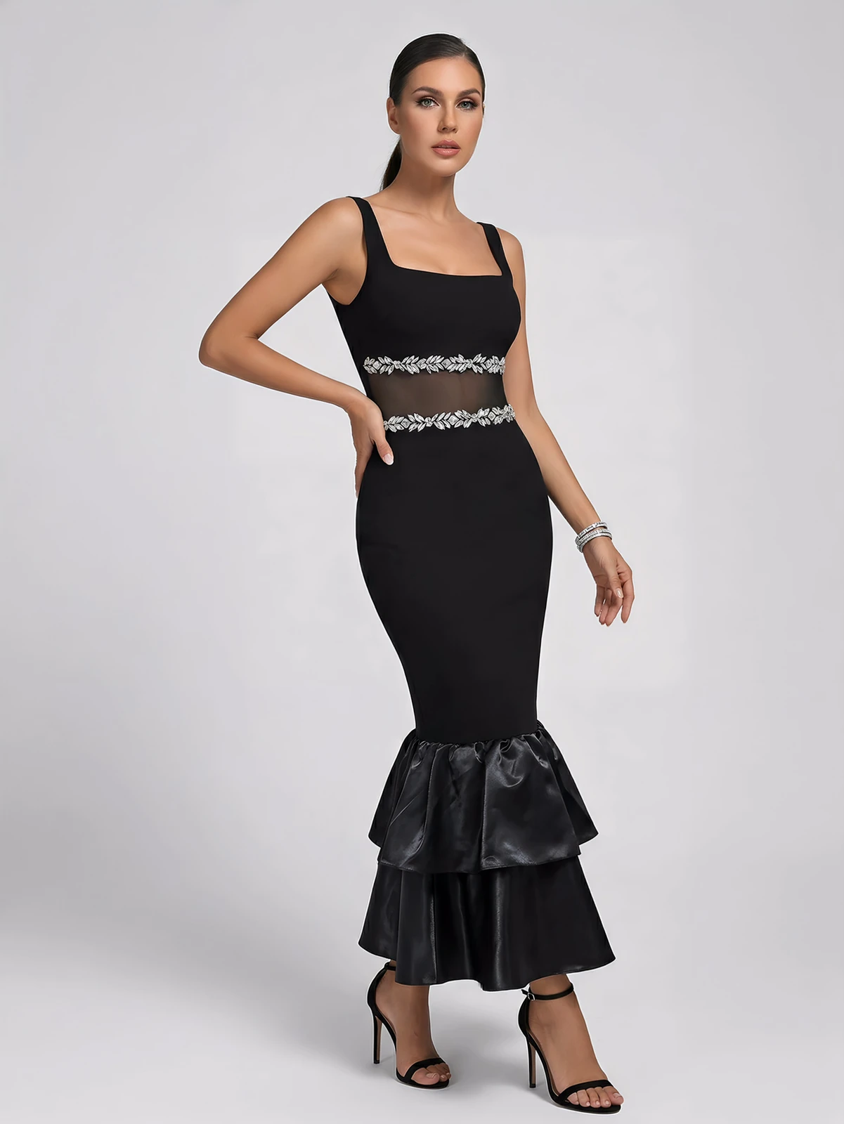 Model posing in black bandage maxi dress showing rhinestone trim and sheer mesh waist insert