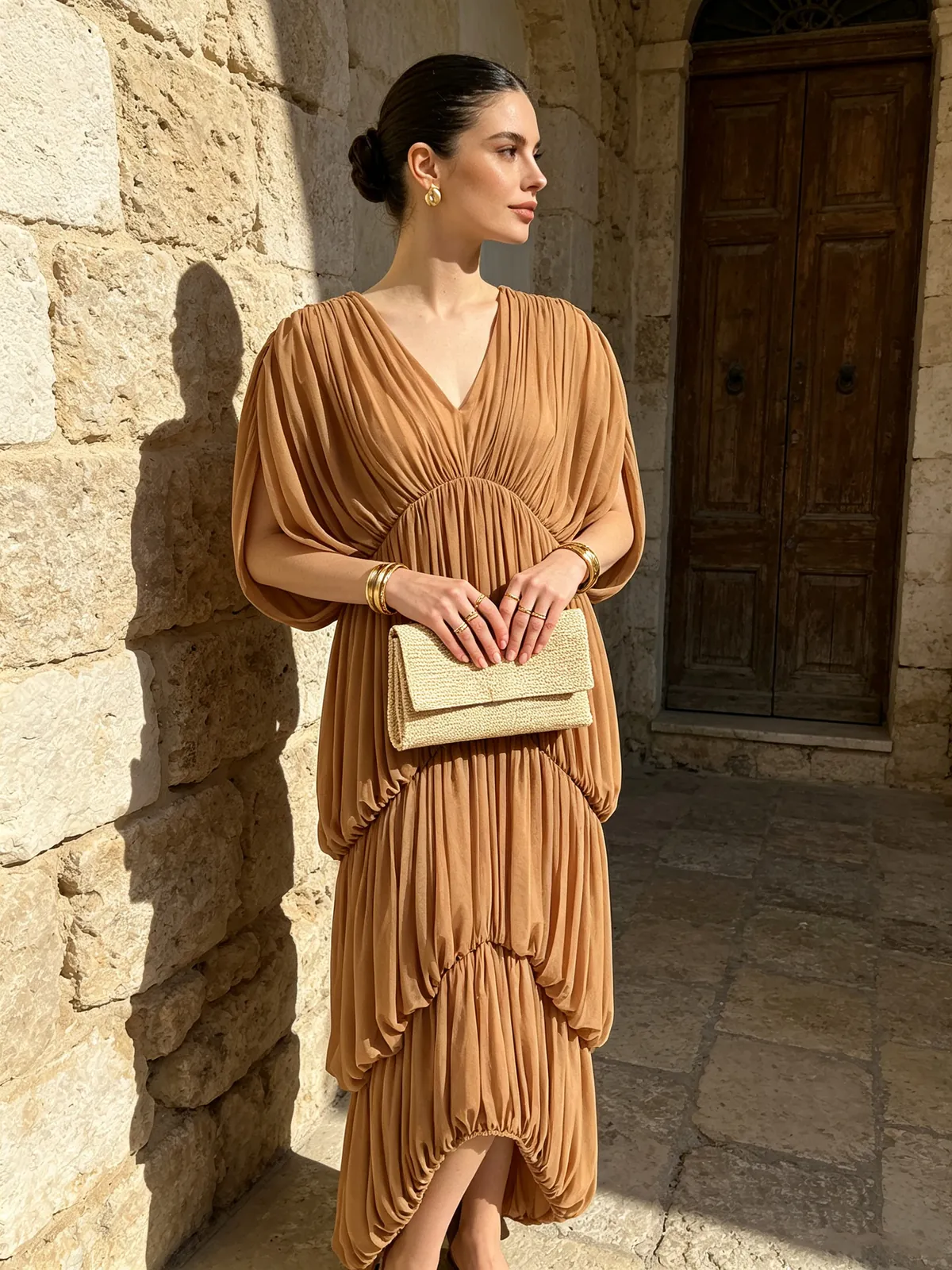 Model in brown deep V tiered ruched maxi dress by a stone wall