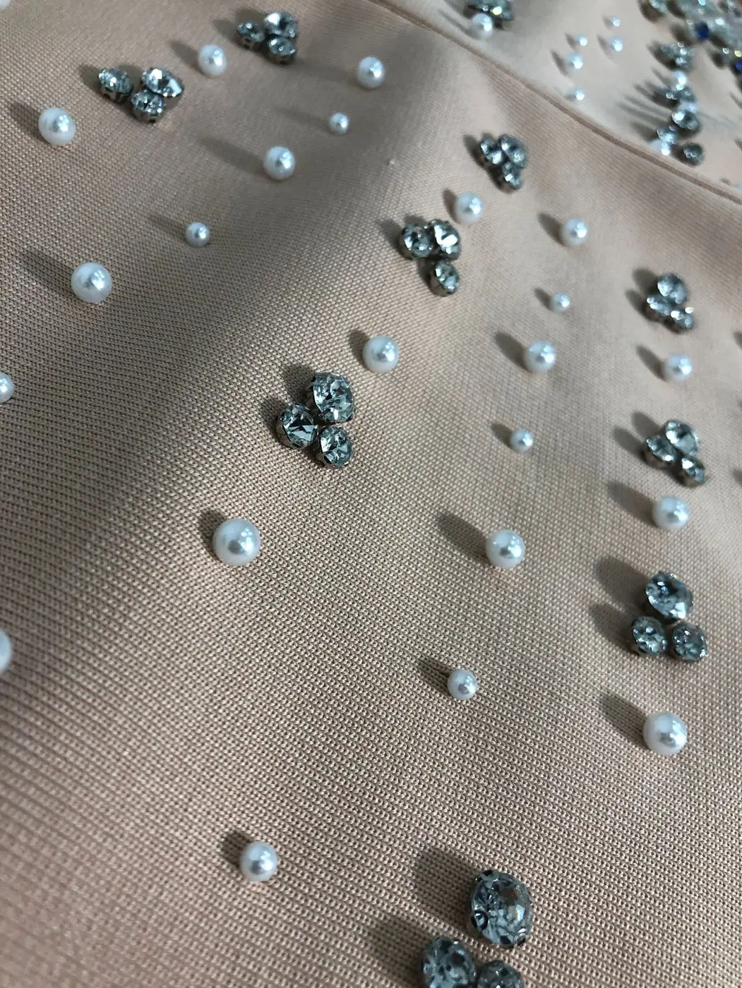 Close-up of rhinestone and pearl embellishment on light orange bandage mini dress